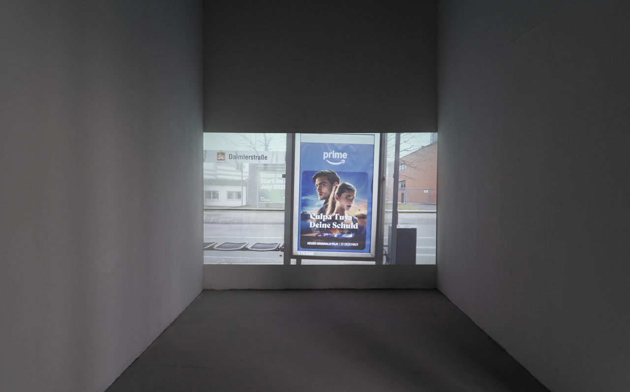 A darkened booth with a video projected onto its back wall: the view out of a window onto a street with a bus stop, parked cars and a lit advertising display.